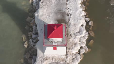 A-red-and-white-lighthouse-in-Southampton-surrounded-by-ice-on-a-sunny-day,-aerial-view