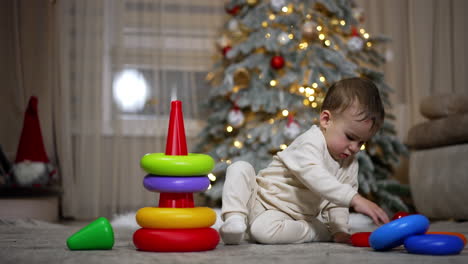 baby playing with stacking rings near christmas tree