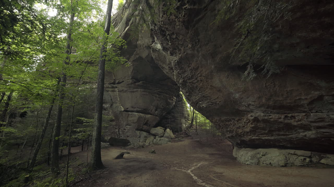excursionista femenina sale de la cueva y bajo un gran arco de piedra natural en el bosque, 4k
