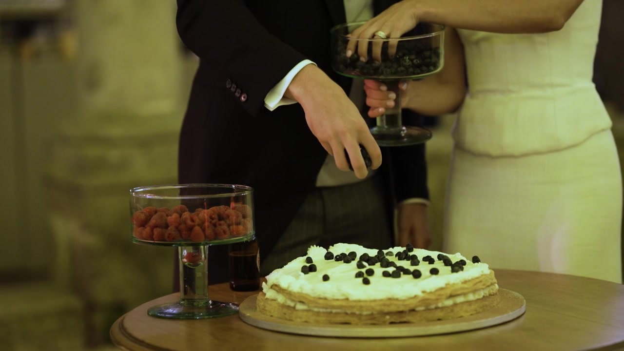 Lagdelt flødekage toppet med blåbær ved siden af skåle med hindbær på et bryllupsdessertbord