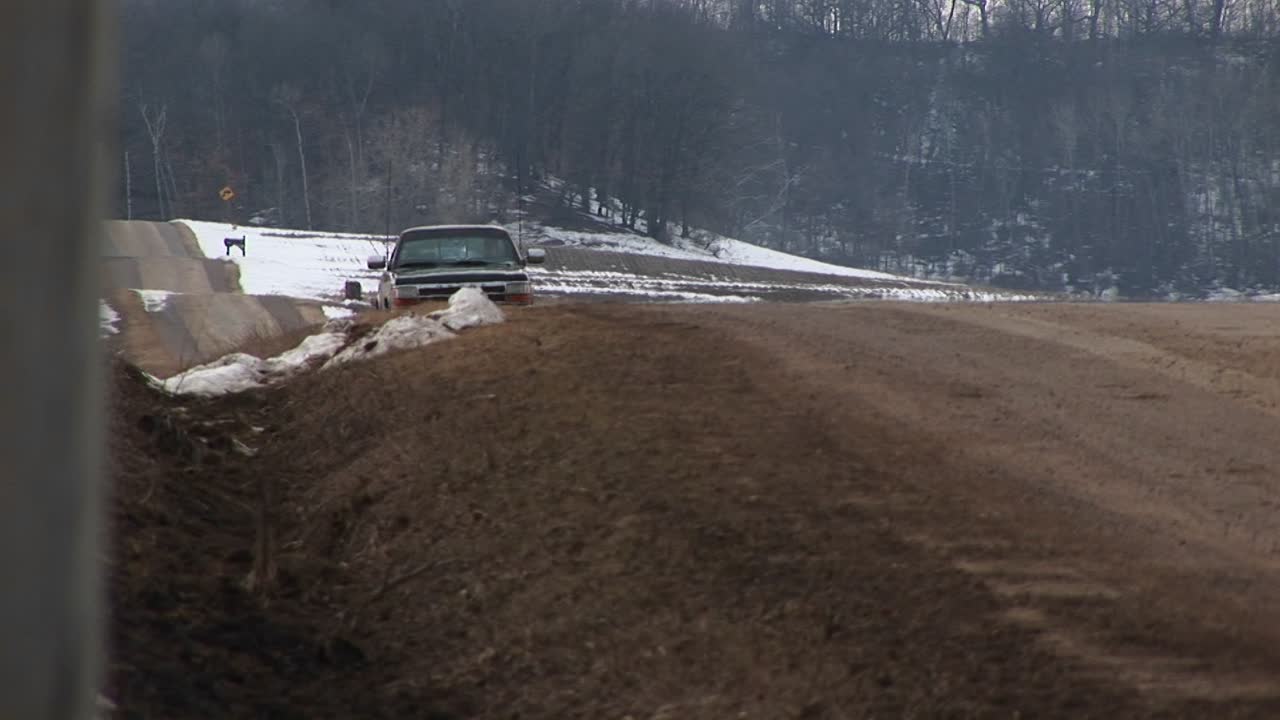 시골의 2차선 도로를 따라 길가 도랑에 설치된 카메라는 상승 위로 시야에 들어오는 픽업 트럭을 포착합니다.