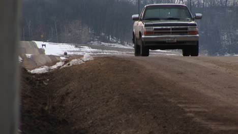 Camera-Placed-In-Roadside-Ditch-Along-A-Rural-Twolane-Road-Captures-A-Pickup-Truck-Coming-Into-View-Over-A-Rise