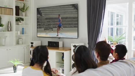 Composite-of-happy-family-sitting-at-home-together-watching-athletics-long-jump-event-on-tv