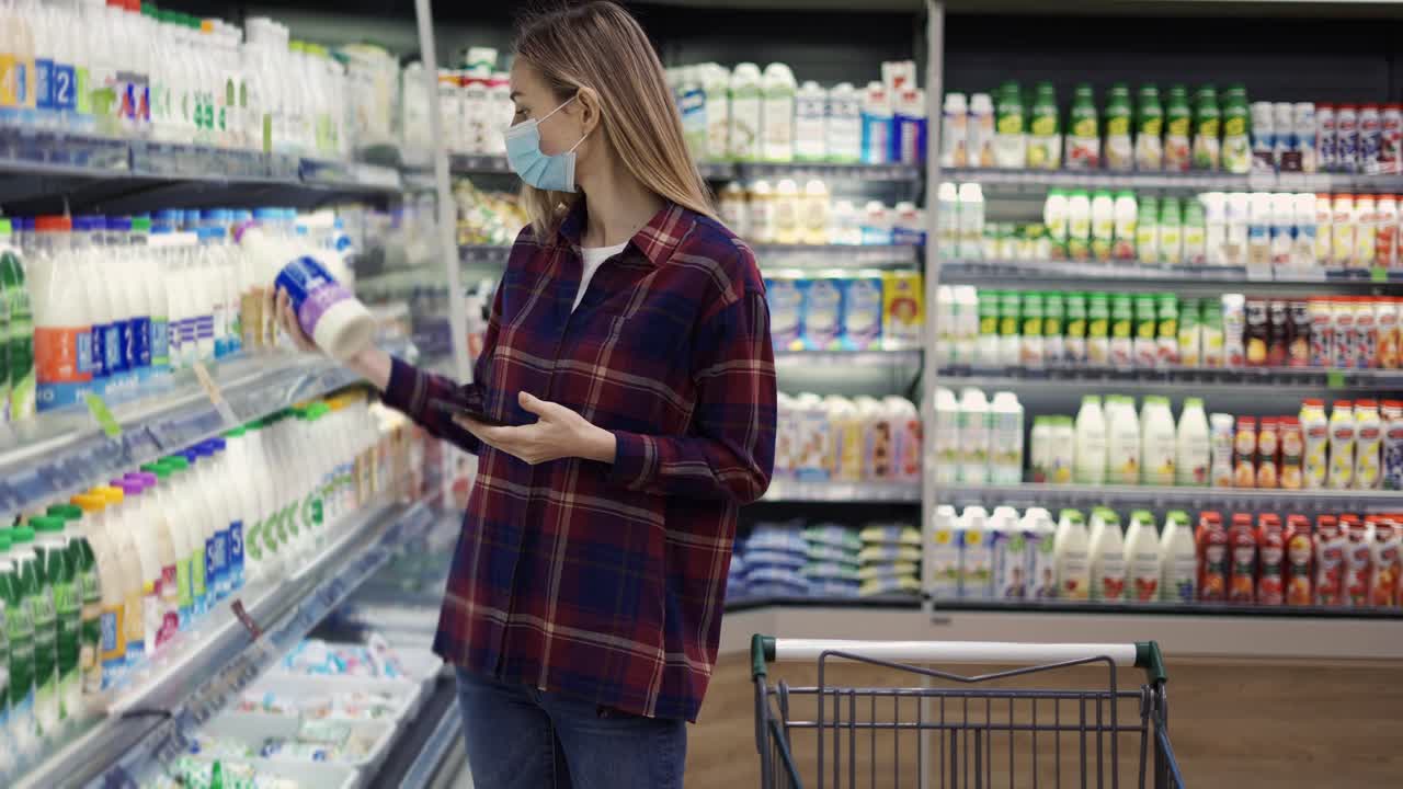 mujer eligiendo leche en el supermercado usando un teléfono inteligente, comprobando la lista de compras