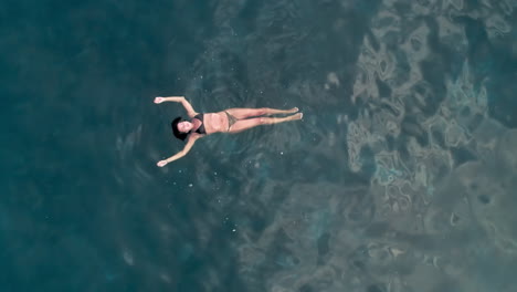 Aerial-birdseye-view-of-woman-swimming-in-the-sea-with-pull-out-higher-into-the-sky