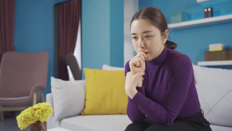 아시아 여성이 거실에 앉아서 불안하고 걱정하고 있습니다.