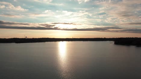 sunset-reflecting-off-a-large-lake-with-calm-water,-aerial-drone