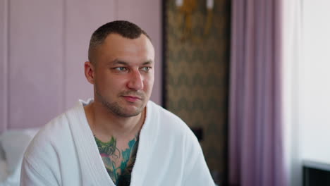 Angry-man-grimaces-sitting-on-bed-in-hotel-room-closeup