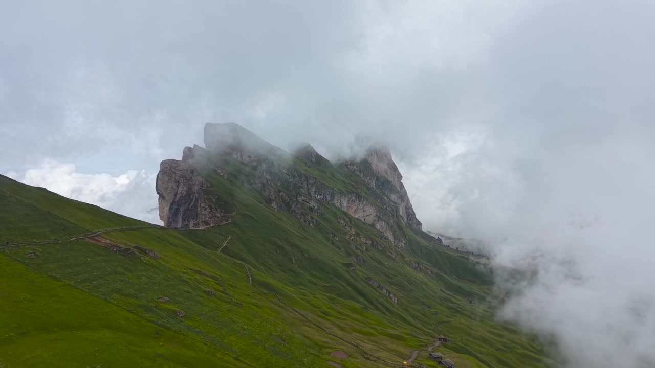 Vista drone della spettacolare cresta del Seceda che si erge sopra rigogliosi prati alpini mentre nuvole basse attraversano le Dolomiti, Italia