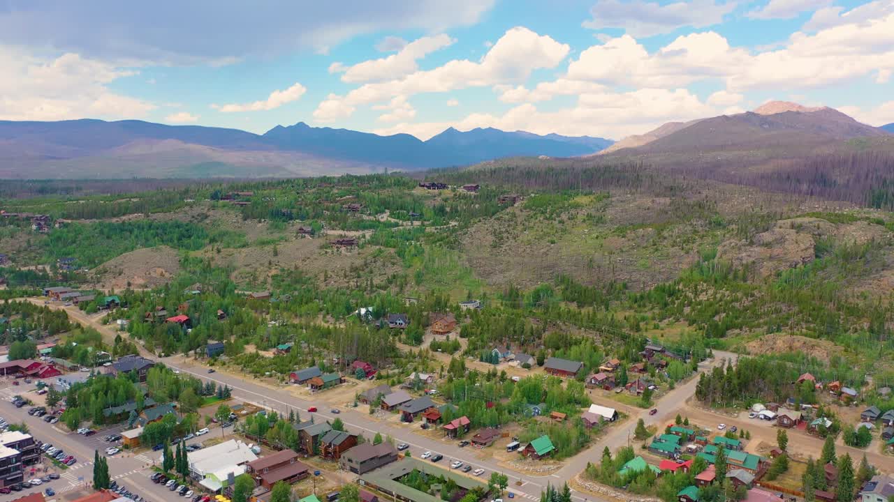 Flyfoto av Big Bear Lake i California med boliger langs skogkledd strandlinje, rolig blått vann, skogkledde halvøyer og fjellterreng som omgir et populært alpinsjøsamfunn under solrike sommerforhold.