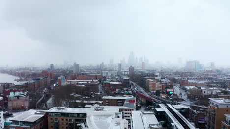 drone shot towards london city centre in snow from limehouse over train tracks dlr