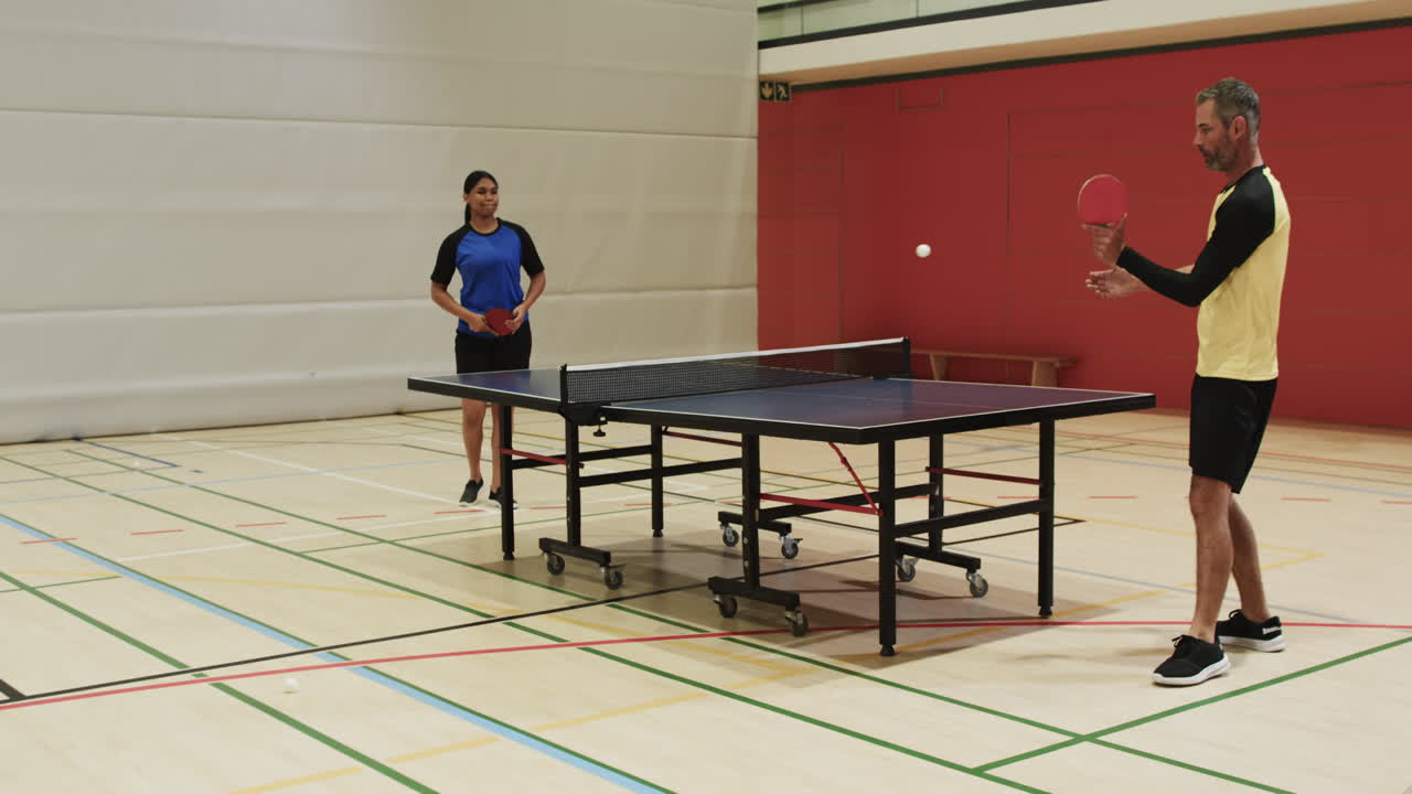 Playing table tennis, man and woman competing in indoor sports hall