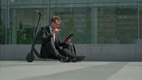 businessman working outside on tablet with scooter