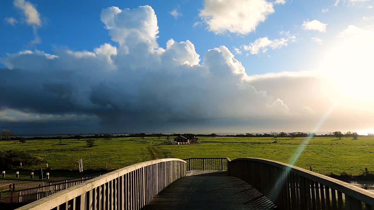 POV Of A Person Walking At Wooden Bridge Towards Countryside Field With Overcast And Stormy Clouds In The Distance. - wide shot