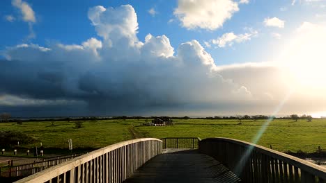 pov of a person walking at wooden bridge towards countryside field with overcast and stormy clouds in the distance. - wide shot