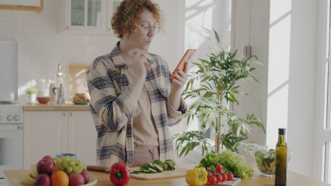 Woman looking at recipe on phone while preparing salad in kitchen