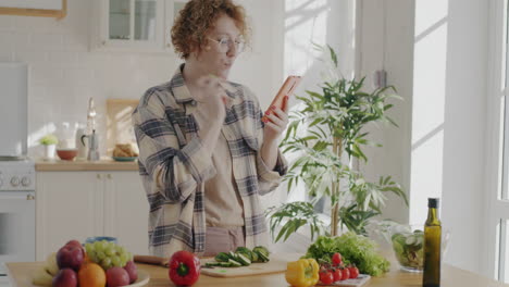 woman looking at recipe on phone while preparing salad in kitchen