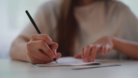 mujer dibuja con lápiz en un libro de ejercicios sentada en la mesa