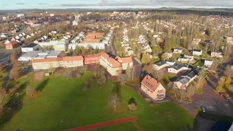 drone footage moving away, while ascending, from some houses and a school in a small town