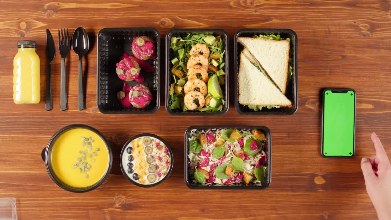 entrega de alimentos vista superior, llevar comidas en contenedores desechables en mesa de madera. cajas de almuerzo con platos vegetarianos cocidos, usando teléfono con pantalla verde croma. dieta saludable. servicio de catering