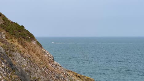 Von-Der-Bray-Head-Cliff-Fährt-In-Der-Ferne-Eine-Yacht-Auf-Dem-Muschelblauen-Meer,-Irland,-Vorbei