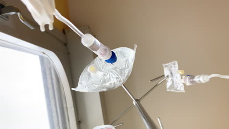 two intravenous drips hang from their stand, administering medication