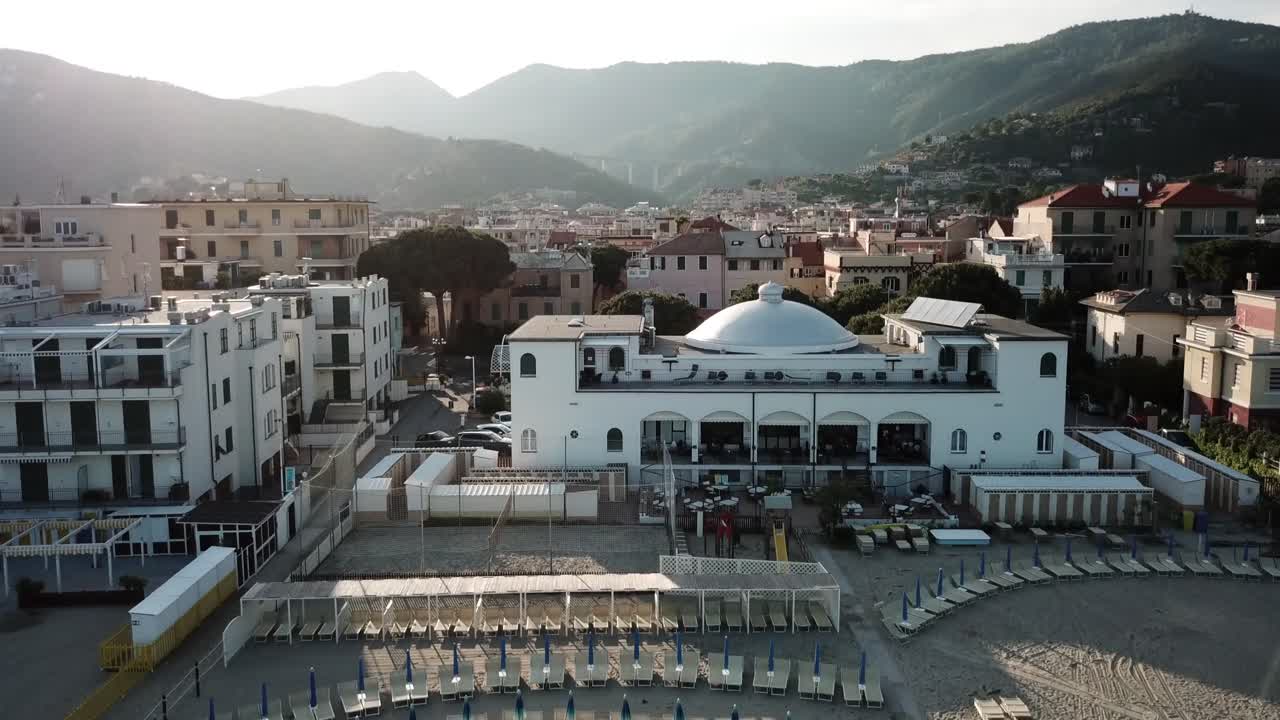 A drone rises in the sky and reveals an italian town next to the Mediterranean during a sunset