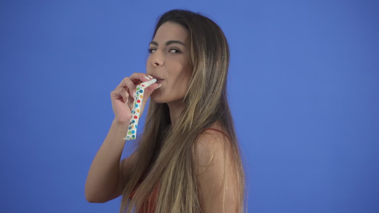 una mujer joven celebra con un soplador de fiesta, cuerno de fiesta