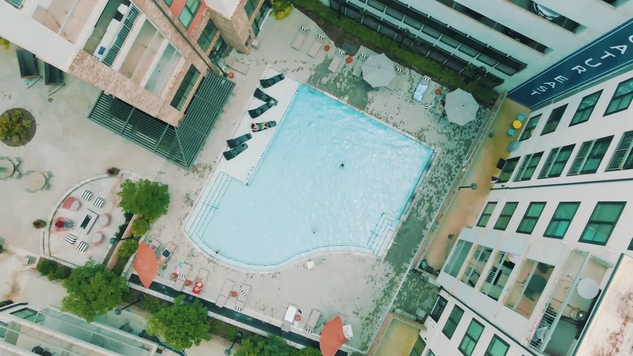Unikke droneoptagelser, der viser et poolområde og en terrasse inde i et stort lejlighedskompleks.
