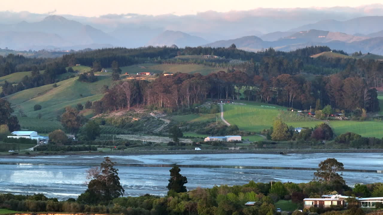 멀리 있는 웅장한 산들에 둘러싸인 푸른 언덕과 물이 있는 큰 집과 저택의 드론 촬영.