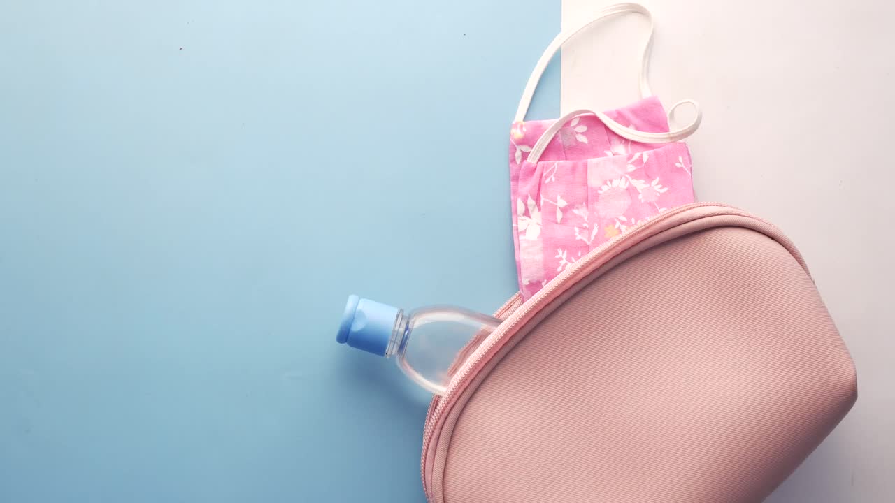 máscara facial rosa y desinfectante de manos en una bolsa de maquillaje