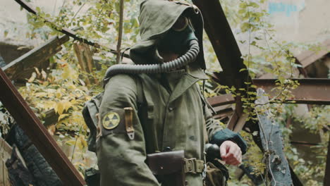 a man wearing a gas mask and protective suit in abandoned house looks readings at the wrist the radi