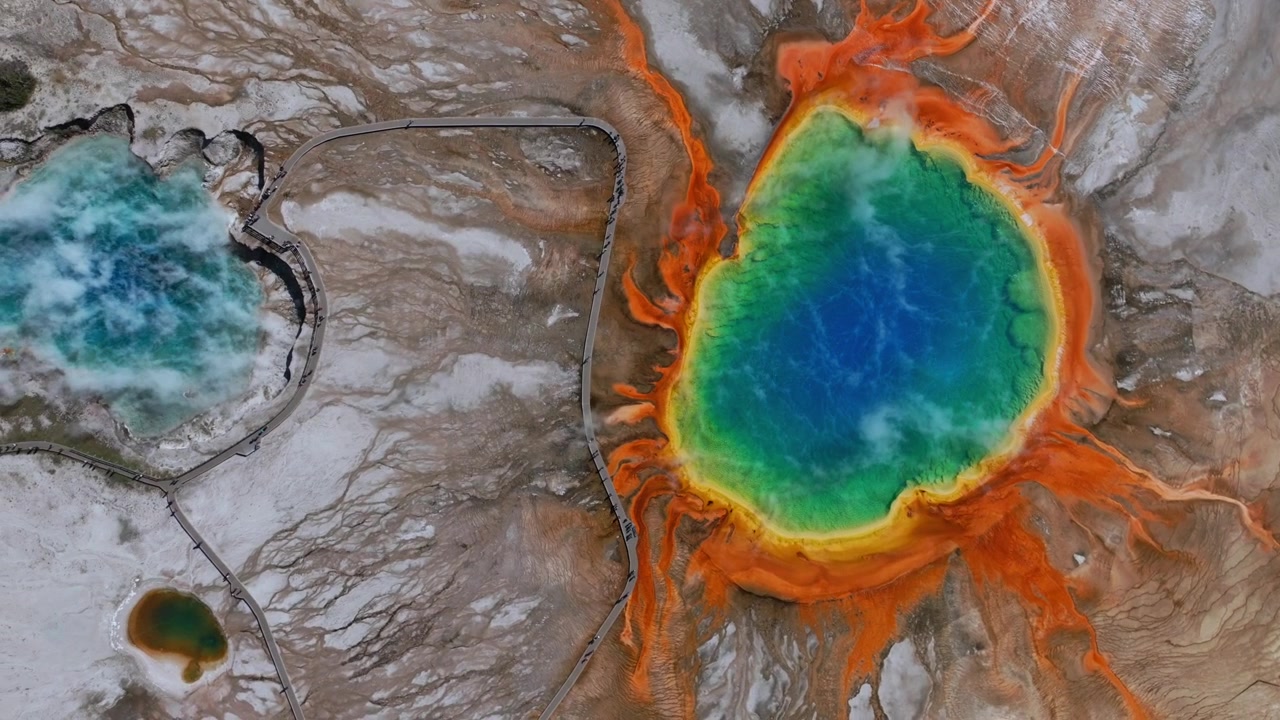 Grand Prismatic Springs, Mid Geyser Basin, lankkupolkua pitkin kulkeva vaellusreitti, Wyomingin Yellowstonen kansallispuisto, ilmakuva droonilla, lintuperspektiivi, luonnonmaisema, pilvinen aamu, värikkäät kuumat lähteet ja altaat vasemmalla.
