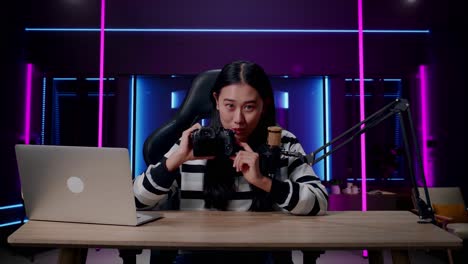 a smiling asian woman with headphone and computer reviewing camera in room lit by neon lights in retro