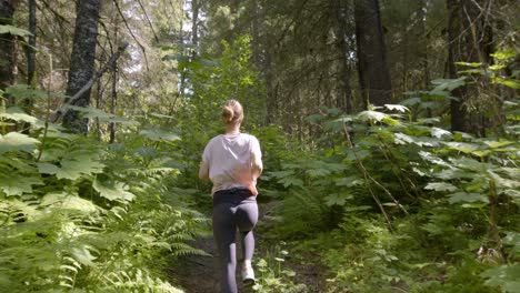 Following-Female-Running-on-Forest-Footpath-in-Wilderness-of-Alaska,-Slow-Motion