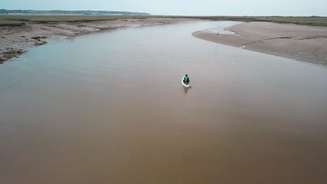 man kayaking on meandering river, drone follows behind and then flies over, camera pans down