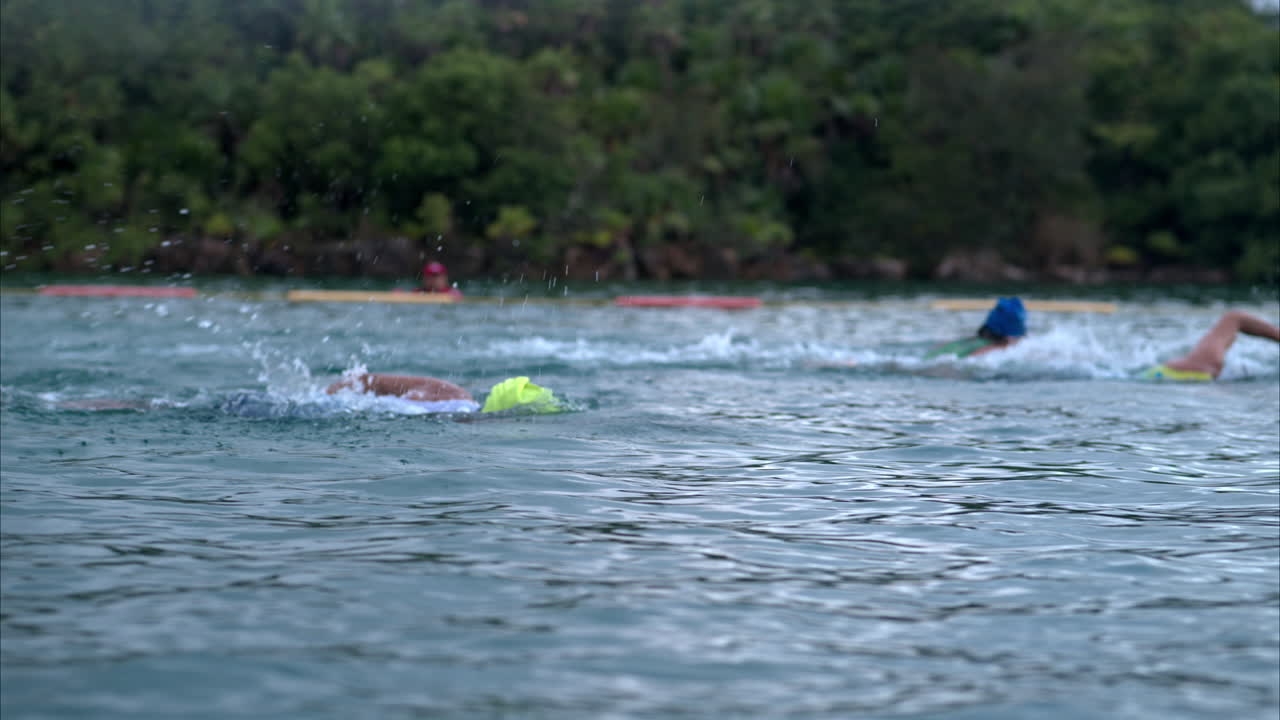 Em câmera lenta, plano médio de um atleta usando touca amarela e óculos de natação, nadando em um triatlo no mar