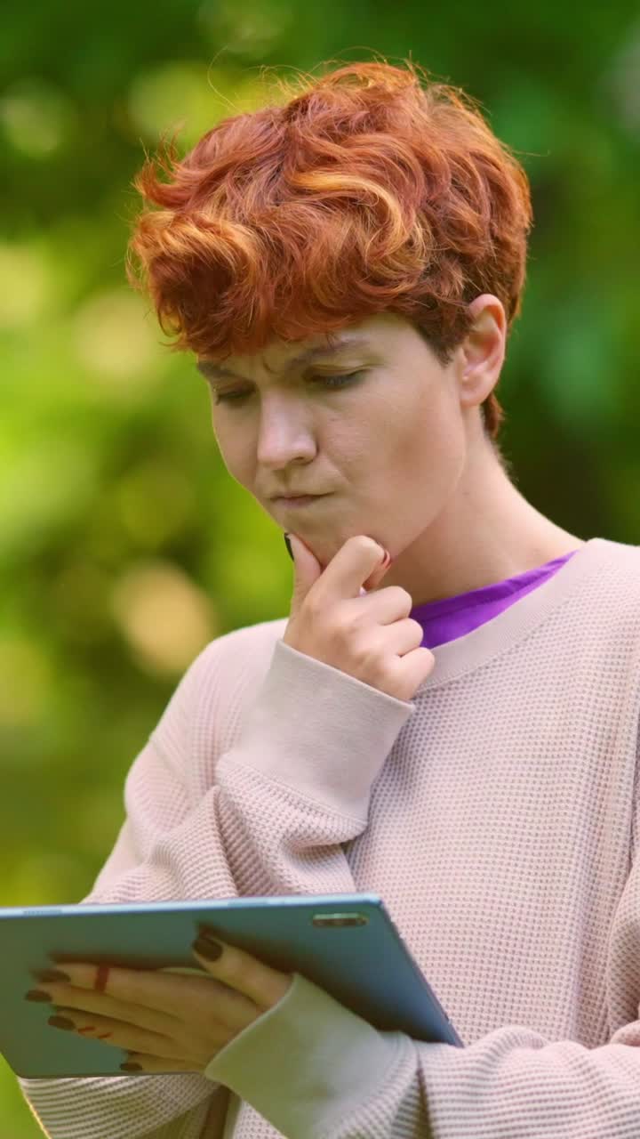 Thoughtful woman with red hair using a tablet outdoors