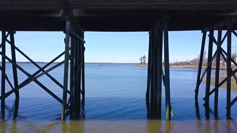 aerial drone looking through and under bridge beams to bay on slough