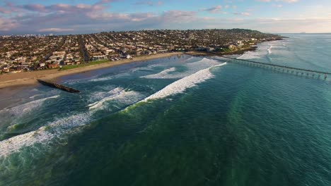 Vista-Amplia-De-Drones-Aéreos-De-4k-Del-Muelle-De-California-Y-La-Costa-De-La-Ciudad-De-Playa,-Enormes-Olas-Azul-Turquesa-Del-Océano-Pacífico-Rodando