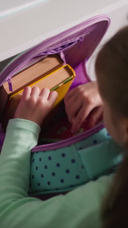 schoolgirl seeks right textbook in schoolbag sitting at desk at home. little girl prepares to do homework in children room after classes at school