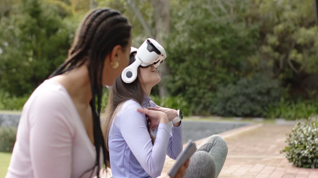Compañeros de trabajo diversos tocando una tablet, guiando a un usuario de realidad virtual que levanta las manos y se estira en el patio del jardín