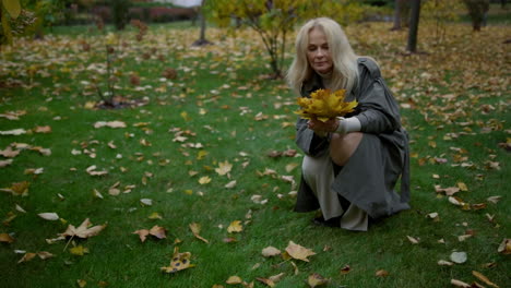 Happy-smiling-woman-taking-yellow-fallen-maple-leaves-from-ground.