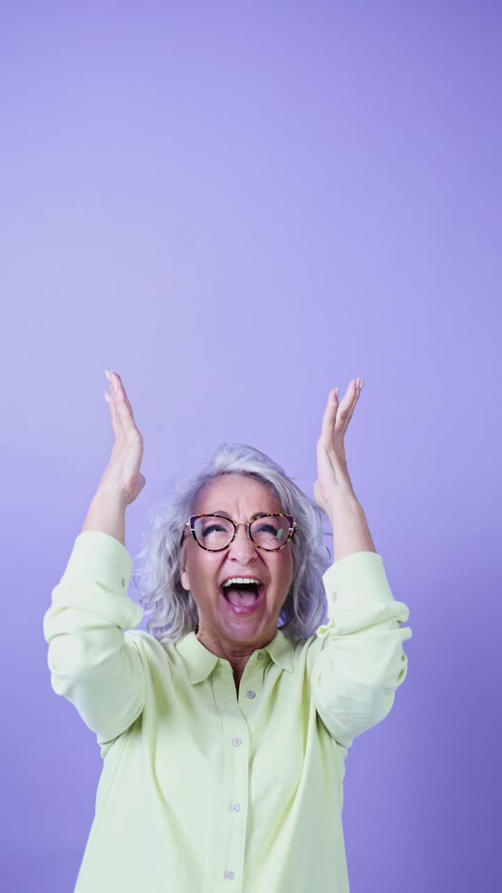 Excited Senior Woman Reacting with Surprise and Joy on Purple Background
