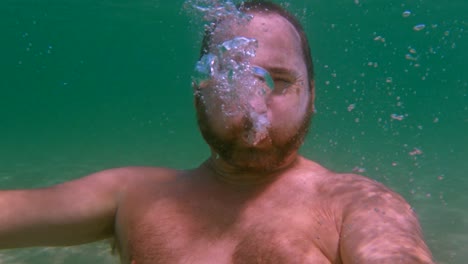 undersea view of bearded man in apnea breathing out air to create bubbles