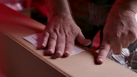 the hands of a male warehouse worker putting an adhesive label with the printed shipping information on a boxed item