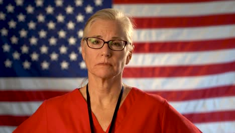 medium tight portrait of a healthcare nurse looking concerned and sympathetic walking towards the camera with an out of focus american flag