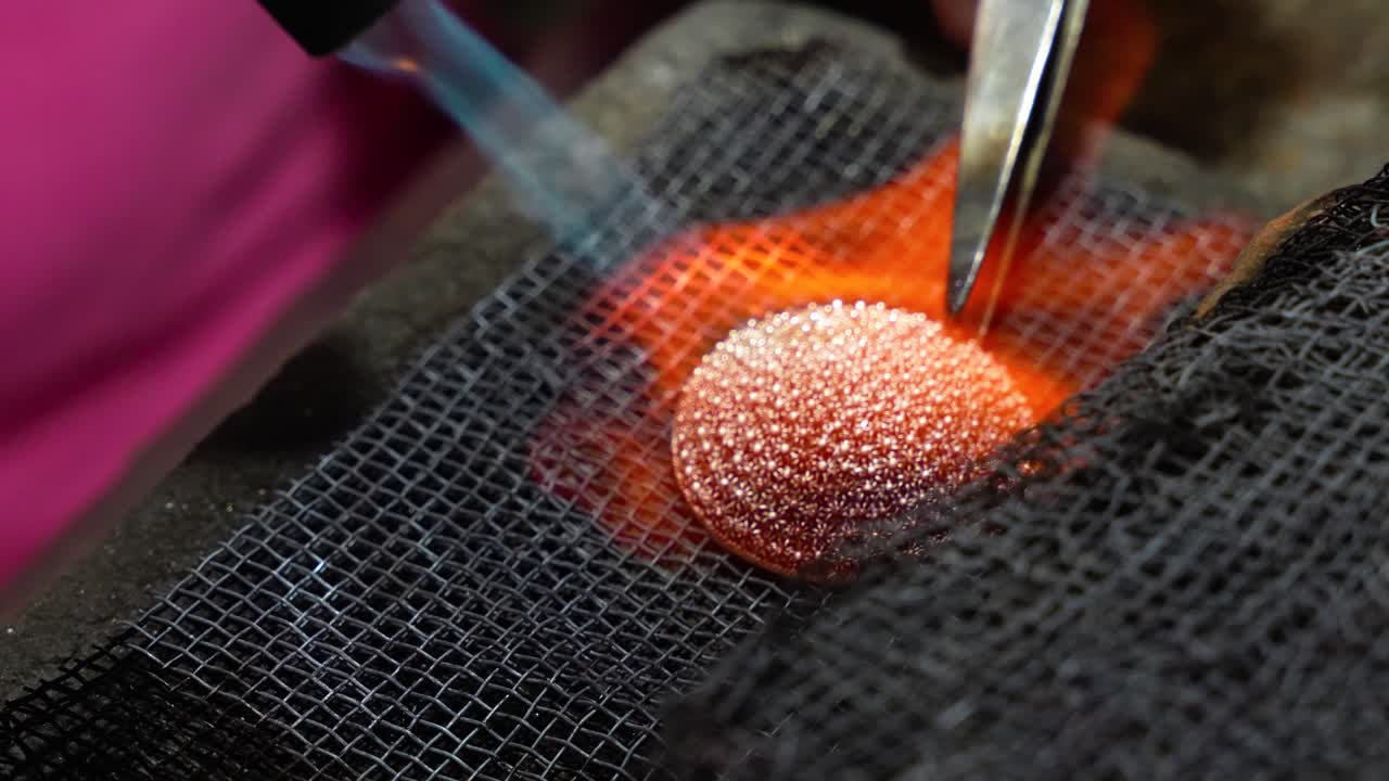 Silversmith at work applying a blowtorch to a piece. Close up