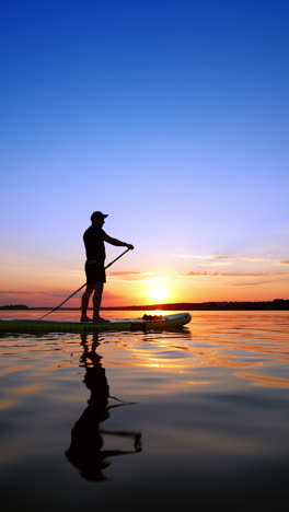 charming sunset on the river in summer. man on the sup board rowing with an oar appears. low angle view. vertical video.