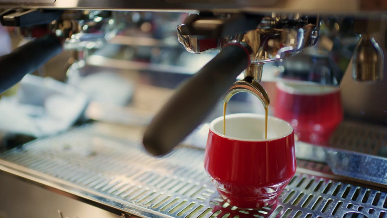 Primo piano di caffè espresso fresco che si versa da una macchina da caffè professionale in una tazza piccola di ceramica rossa.